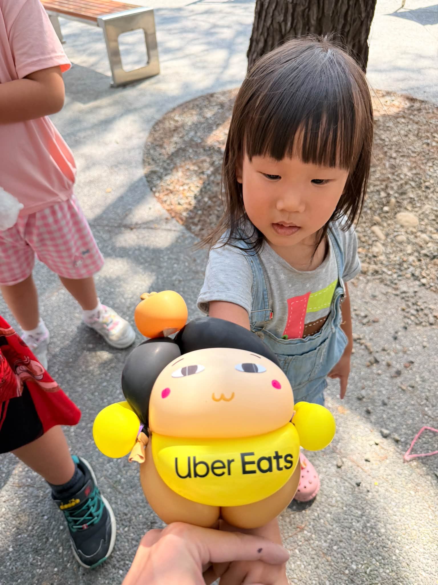 穿吊帶褲的小女孩好奇盯著遞到面前的 Uber Eats 娃娃造型氣球