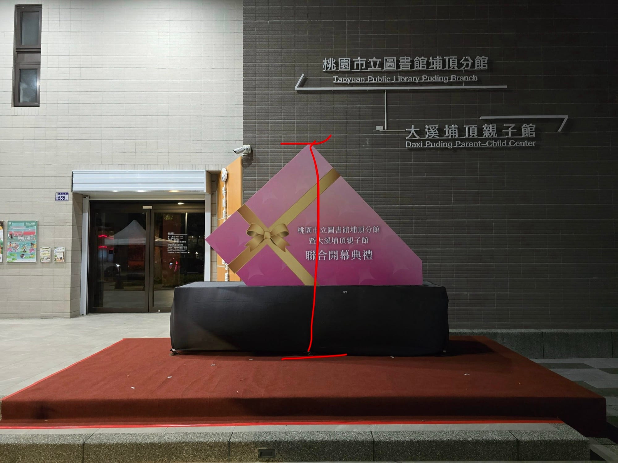 夜裡的現場，黑布包住的舞台前立著粉紫色禮物盒造型背板，上面畫著紅色線條