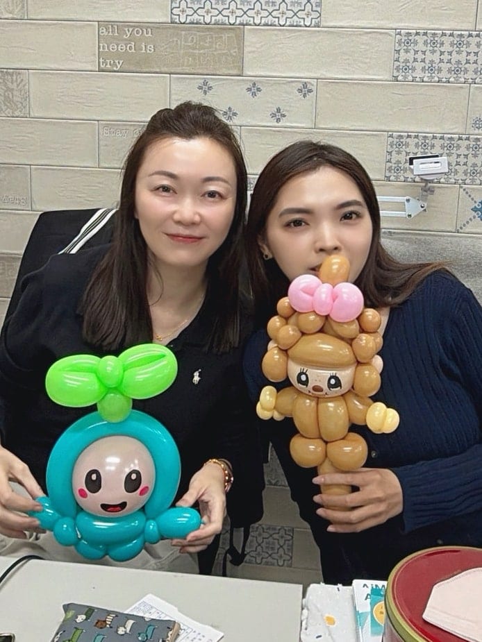 兩位女士坐在磁磚牆前,各捧著芽芽氣球和萌琪琪氣球