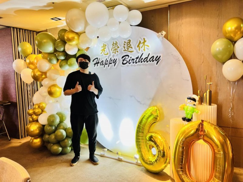 黑衣男士在莫蘭迪綠金白氣球拱與光榮退休背板前比讚，旁邊是金色 60 數字氣球