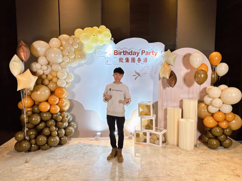 柯男站在入口拍照區背板前,兩側是咖啡、焦糖橘、米白色不規則氣球柱
