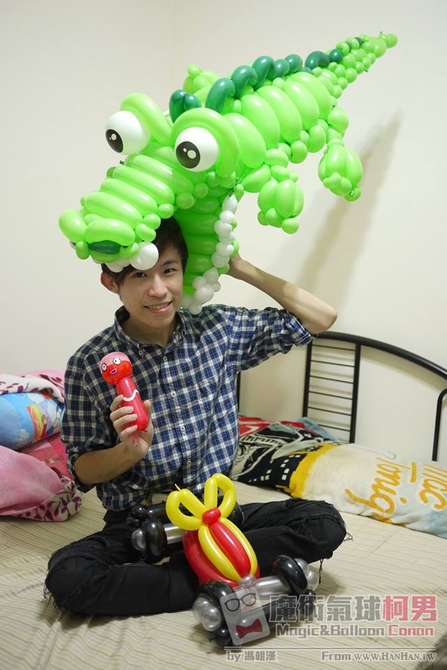 巨型綠色鱷魚造型氣球帽，鱷魚張嘴咬住柯男的頭，旁邊是紅色小人與禮物車造型